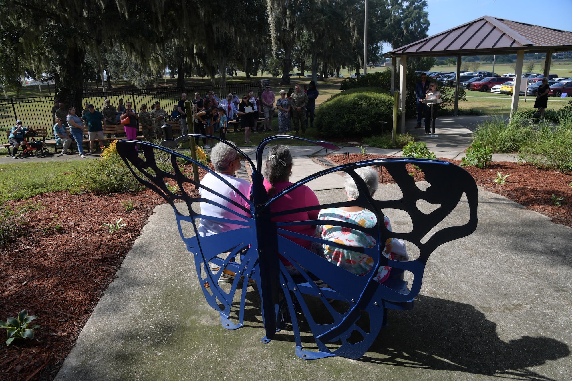 A metal butterfly shaped chair sits in the middle of a gathering.
