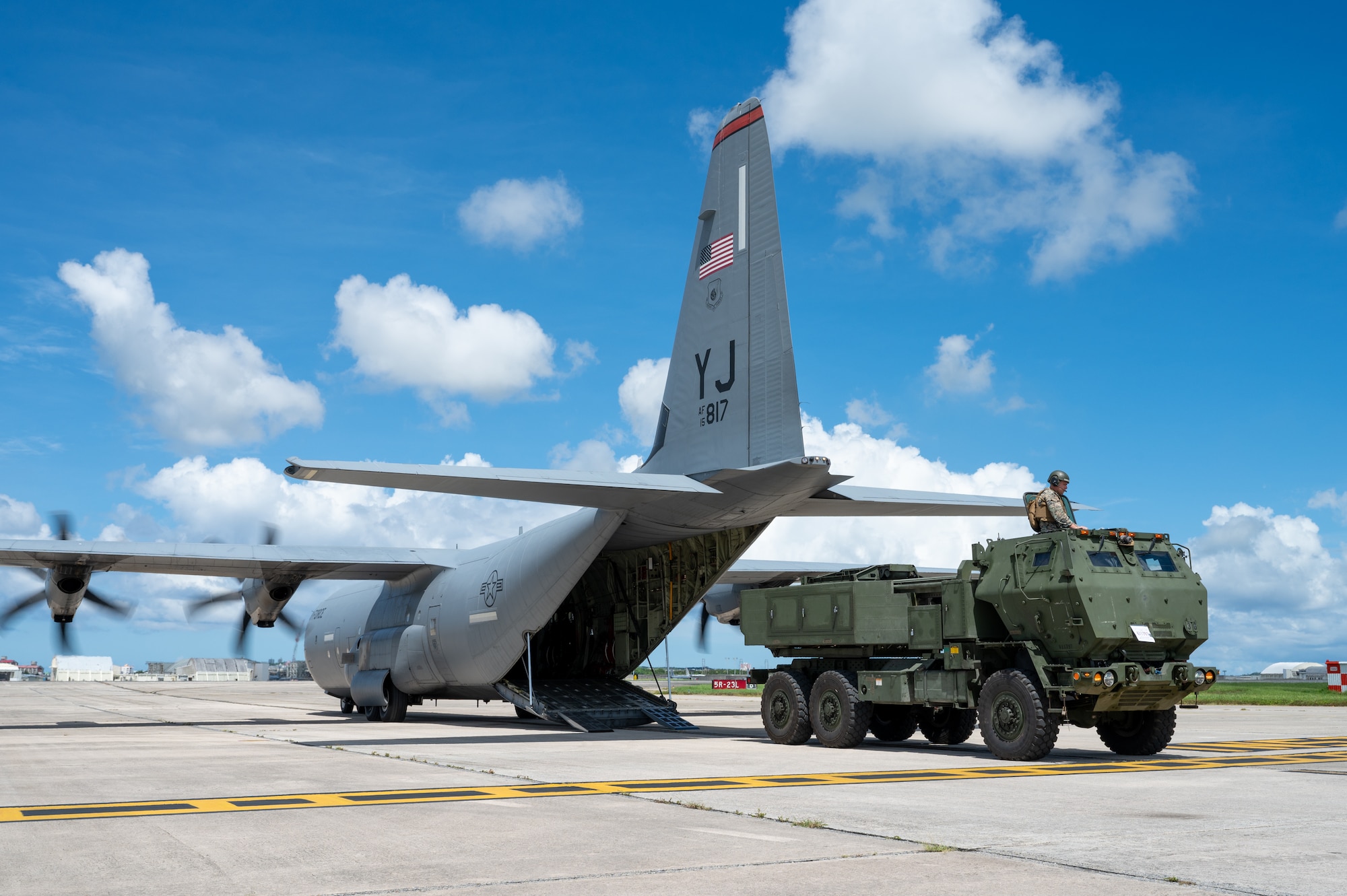 A U.S. Marine Corps High Mobility Artillery Rocket System sits on the flight line prior to being loaded into a U.S. Air Force C-130J Super Hercules assigned to the 36th Airlift Squadron during a HIMARS Rapid Insertion training at Kadena Air Base, Japan, Sept. 18, 2025. The training gave personnel an opportunity to practice emerging tactics, techniques and procedures that allow C-130 aircrews to reload ammo pods into a HIMARS without any material handling equipment, such as K-loaders and forklifts, in a process known as HIMARS Direct Reload Inside Plane. This marked the first time on record that a Mobility Air Force aircrew within Pacific Air Forces has executed HIDRIP, as the 36th AS continues to develop homegrown training events designed to refine the skills needed to support operations in austere environments. (U.S. Air Force photo by Staff Sgt. Natalie Doan)