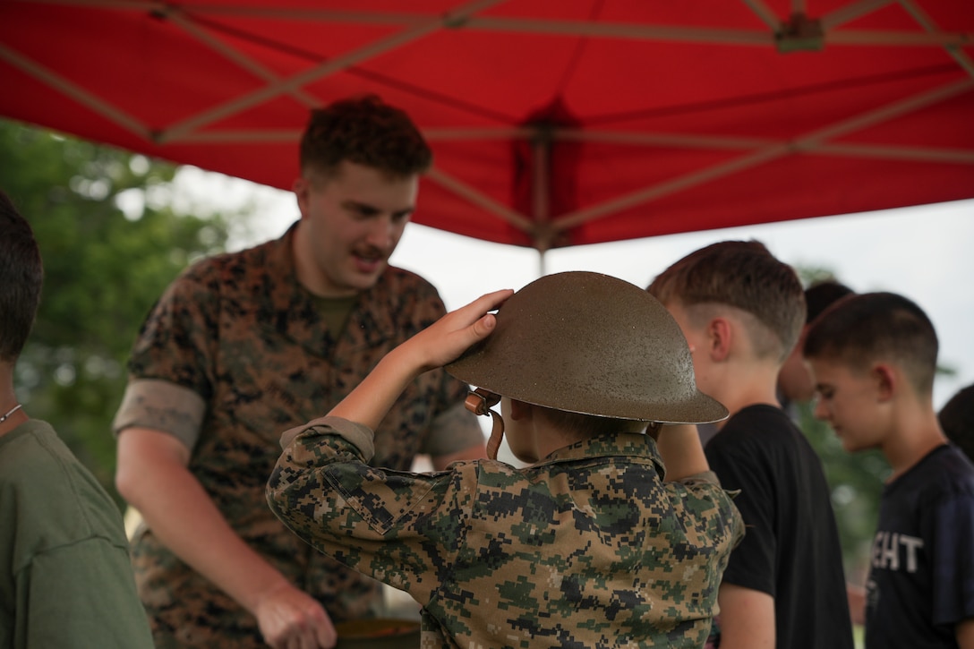 U.S. Marine Lance Cpl. Charles Devoll, a volunteer with Marine Corps University, shows historical uniform items displayed by the National Marine Corps Museum to participants at Marine Corps Community Service’s Future Marine Bootcamp on Marine Corps Base Quantico, Virginia, Sept. 23, 2025. This “boot camp” is designed to give school-aged children a glimpse of life as an enlisted Marine while simultaneously emphasizing the importance of community. In another sense, the event also helped the kids to better understand their parents, family, or friends that serve. (U.S. Marine Corps photo by Lance Cpl. Hannah Kear)