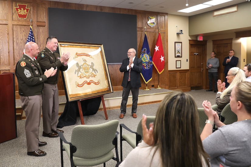 A ceremony marks the return of a historic flag from more than 100 years ago to Pennsylvania National Guard headquarters September 29, 2025, at Fort Indiantown Gap, Pennsylvania. Joseph Reselli, an electrician and lifelong Pennsylvanian who purchased the flag and donated it, presented the flag to Maj. Gen. John R. Pippy, Pennsylvania’s adjutant general, and Command Sgt. Maj. Shawn Phillips, command senior enlisted advisor. It is believed to date from 1920-21, soon after the National Defense Act of 1920 reorganized the U.S. armed forces and formally designated the National Guard, which had previously been known as militias. (U.S. Army National Guard photo by Zane Craig)