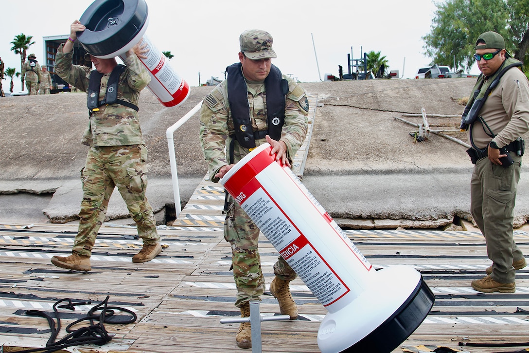 Two service members move red and white buoys along a shoreline.