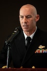 A Navy chaplain speaks into a microphone with his eyes lowered.