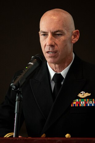A Navy chaplain speaks into a microphone with his eyes lowered.