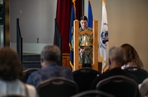 A female Navy Officer rings a large bell in front of a crowd