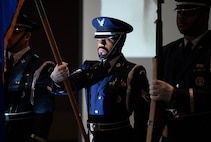 An honor guard member holds a flag away from his body with light from a projector shining on his face.