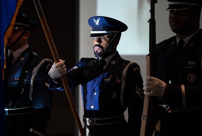An honor guard member holds a flag away from his body with light from a projector shining on his face.