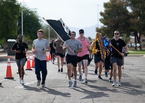 U.S. Air Force Airmen assigned to the 56th Fighter Wing carry a POW/MIA flag and squadron guidons while running laps during the 24-hour POW/MIA remembrance run, Sept. 18, 2025, at Luke Air Force Base, Arizona. The event honors prisoners of war and those missing in action, ensuring their sacrifice is never forgotten. Runners kept the POW/MIA flag moving for a full day to show America’s resolve to bring every service member home. (U.S. Air Force photo by Airman Rebecca Wagner)