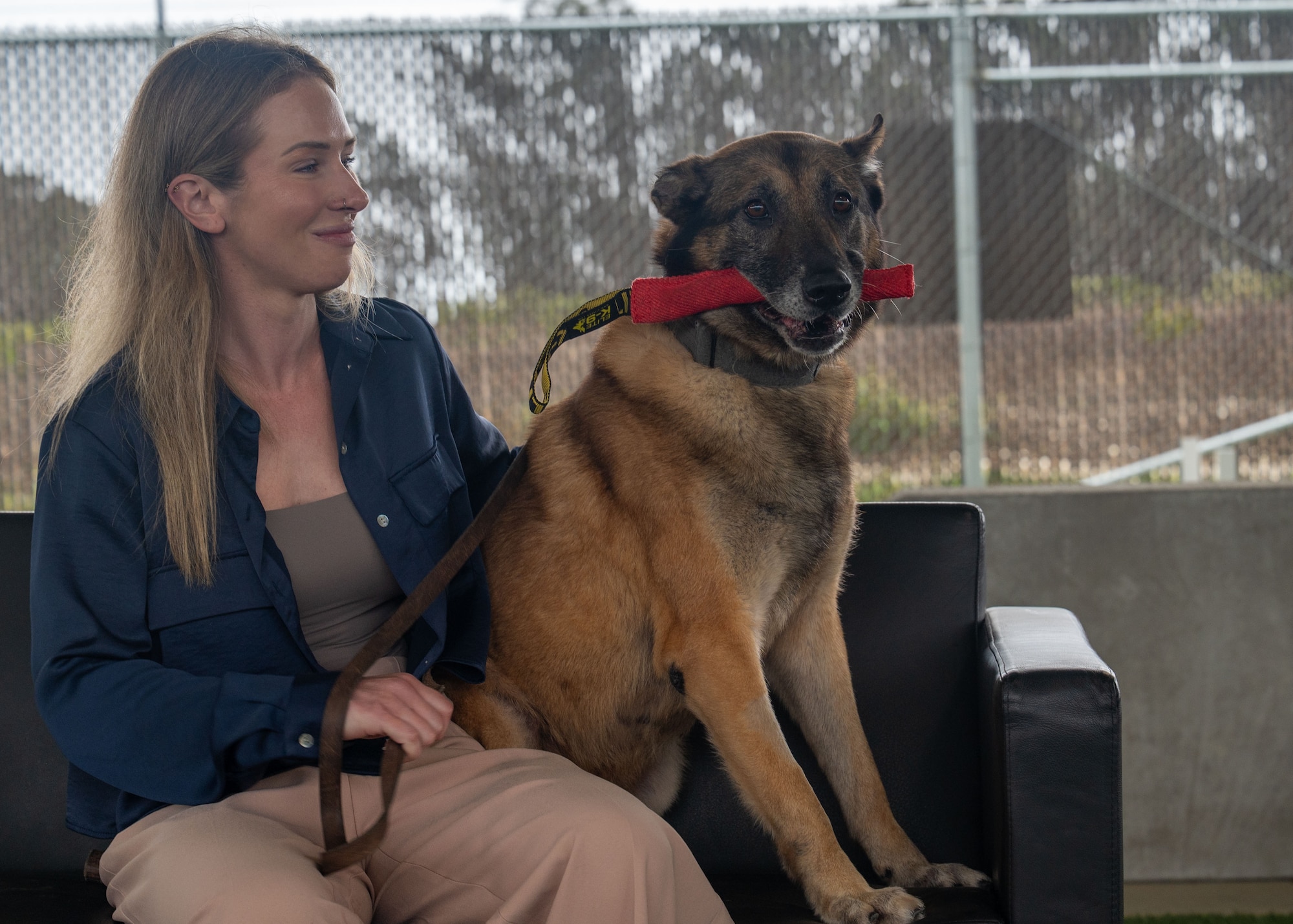 A woman pets a dog. They are sitting on a bench. The dog has a chew toy in his mouth.