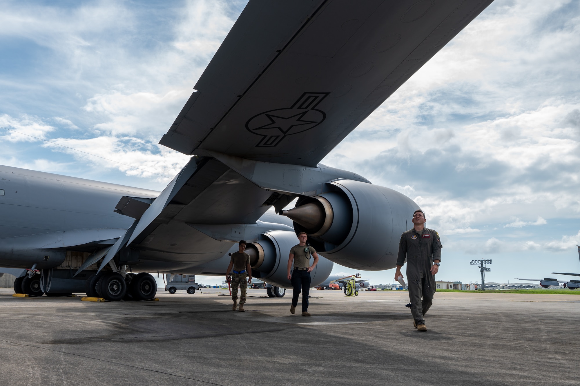 military members walk underneath the wing of a KC-135 while it is parked
