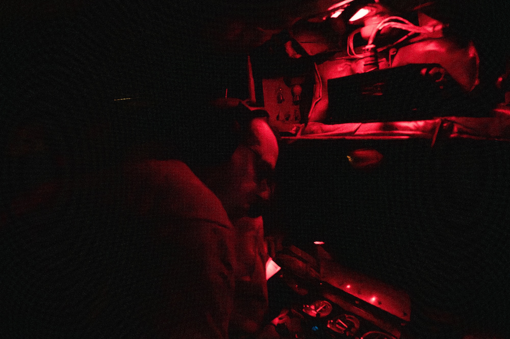 military member lays in a boom pod in red light