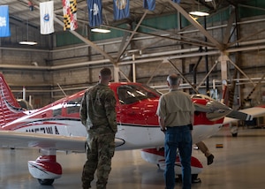 Two men stand in front of a red plane