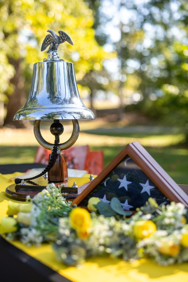 The ceremonial bell, U.S. flag and flowers are displayed during the Bells Across America ceremony at the Lejeune Memorial Gardens in Jacksonville, North Carolina, Sept. 25, 2025. The ceremony was held as part of the Navy Gold Star Program to honor and remember the sacrifice of fallen service members and provide long-term support to their surviving families. This ceremony was the first of its kind in the state of North Carolina. (U.S. Marine Corps photo by Lance Cpl. Alyssa J. DeCrane)
