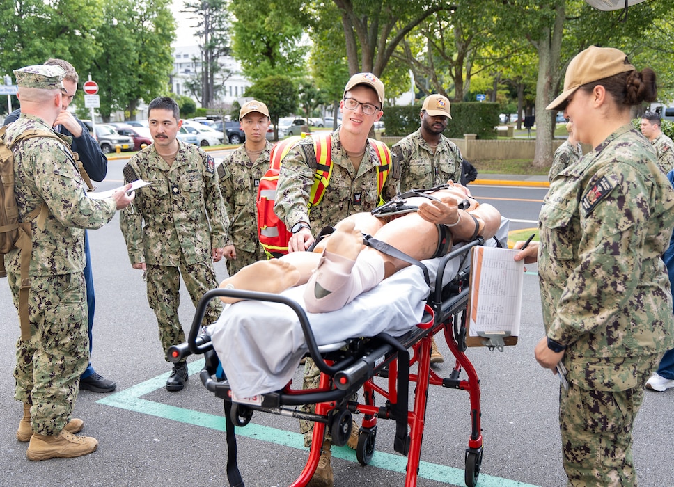 250923-N-SK815-1050 YOKOSUKA, Japan (Sept. 23, 2025) –Hospital Corpsman 3rd Class Evan Talcott, assigned to U.S. Navy Medicine Readiness and Training Command (USNMRTC) Yokosuka, transfers a simulated casualty from an U.S. Navy Medicine Readiness and Training Unit (USNMRTU) Atsugi ambulance during a mass casualty drill. The patient was prepped by a medical crew from USNMRTU Sasebo for medical evacuation to Naval Air Facility (NAF) Atsugi and then to USNH Yokosuka. (U.S. Navy photo by Ai Hazama)