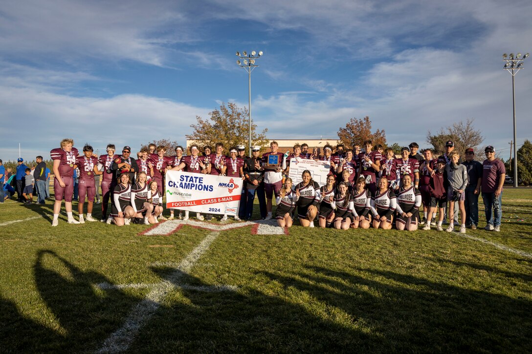 U.S. Marine Corps Sgt. Maj. Pablo Alarcon, Sergeant Major for Recruiting Station Albuquerque, and U.S. Marine Corps Sgt. Tyler J. Fisher, a recruiter with Recruiting Sub-Station Roswell, Recruiting Station Albuquerque, pose for a group photo during the Melrose High School Vs. Mesilla Valley Christian School football game at Melrose High School in Melrose, New Mexico, Nov. 23, 2024. Marines with Recruiting Station Albuquerque had the opportunity to conduct the coin toss at the beginning of the game, as well as hold a recruiting booth to provide more information about service in the Marine Corps. (U.S. Marine photo by Sgt. Mark A. Morales)