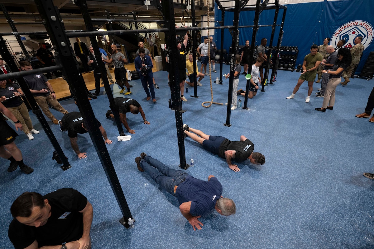 A group of men and women in athletic attire are doing pushups, while others observe in an indoor gymnasium.