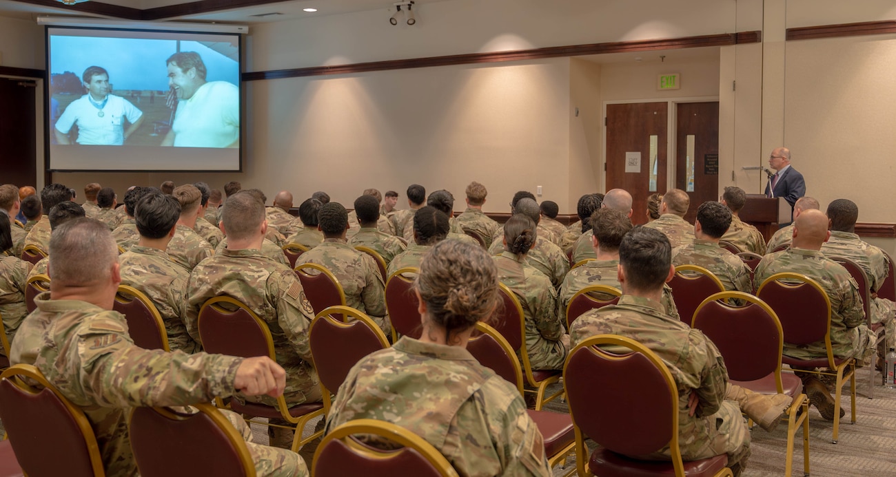A room full of Airmen listen to a speaker.