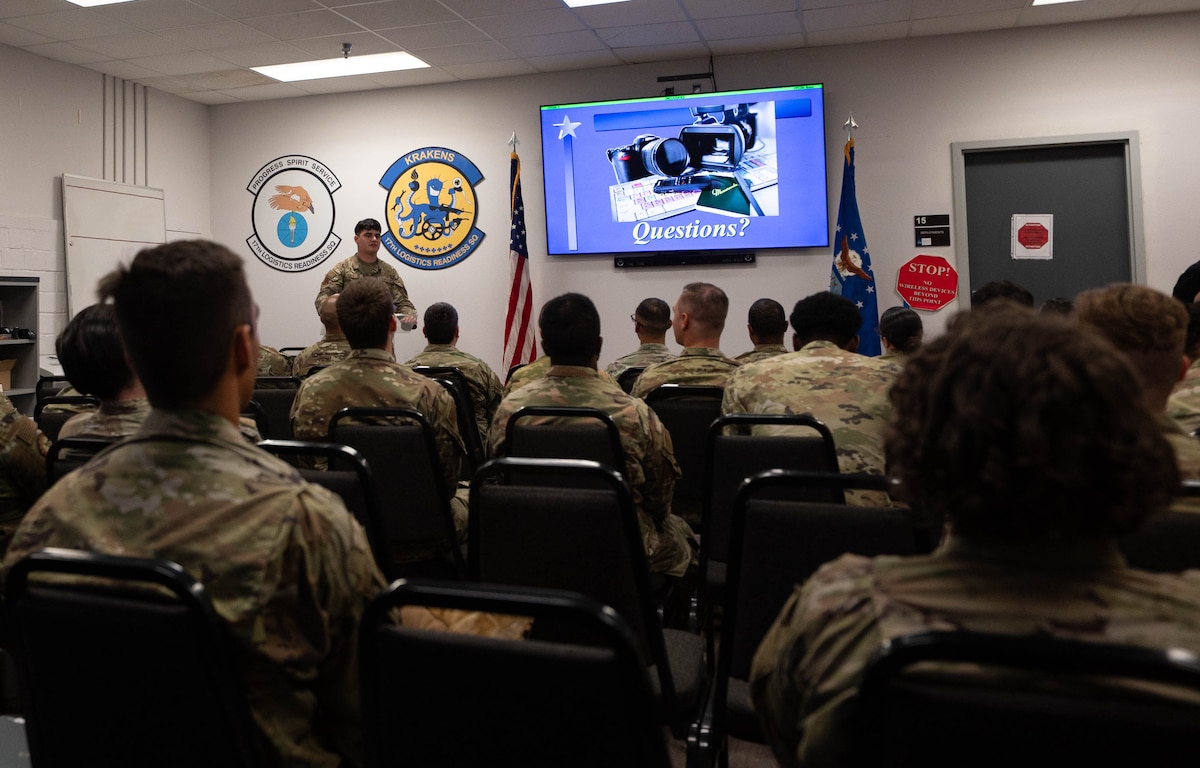 A man in an Air Force camouflage uniform stands in front of numerous service members while giving a brief.