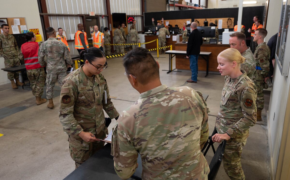 A women in an Air Force camouflage uniform receives information by a women and man in uniform regarding religious services.