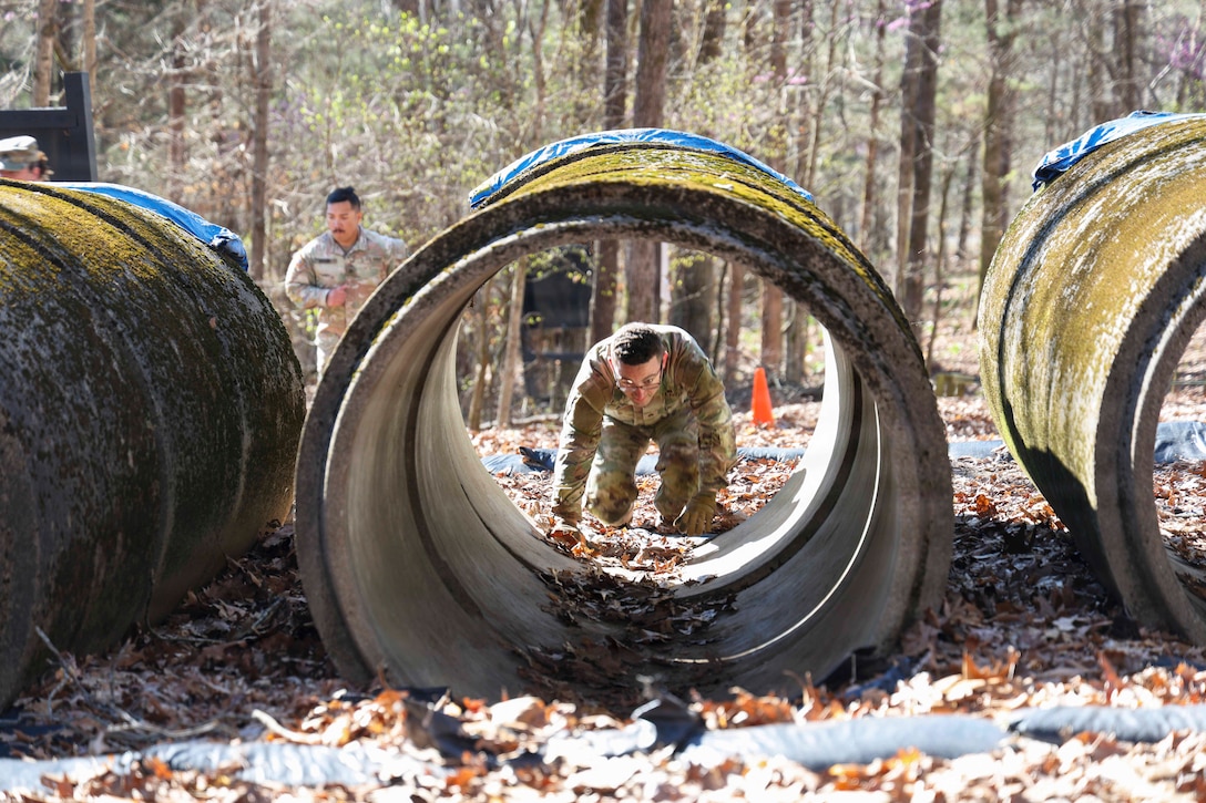 A soldier prepares to crawl in a tunnel surrounded by leaves in the woods during the day.
