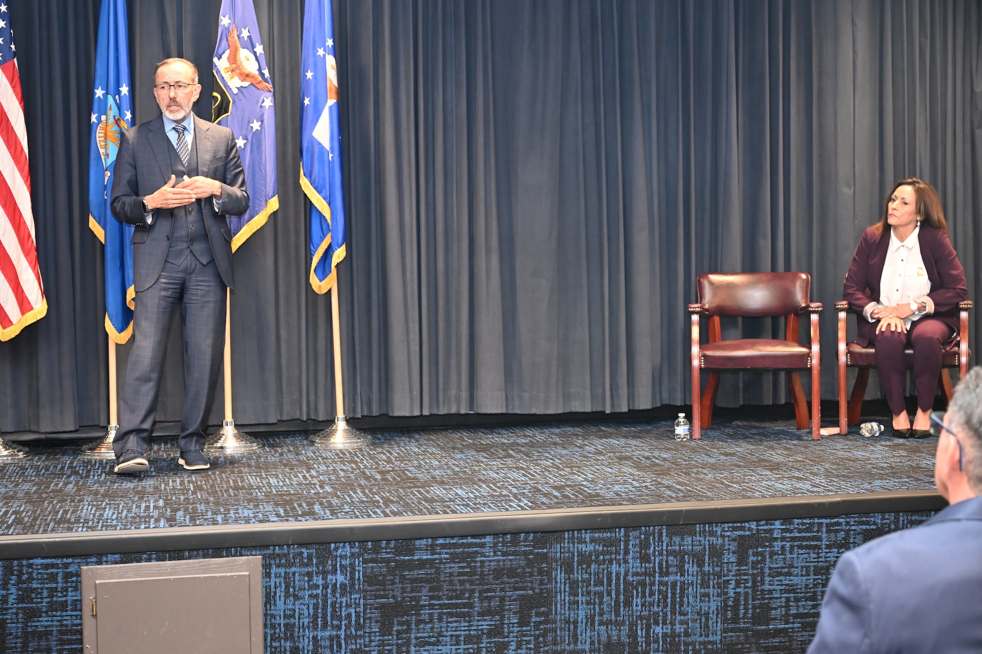 A man in a suit presents a flag in a case to a woman in a suit