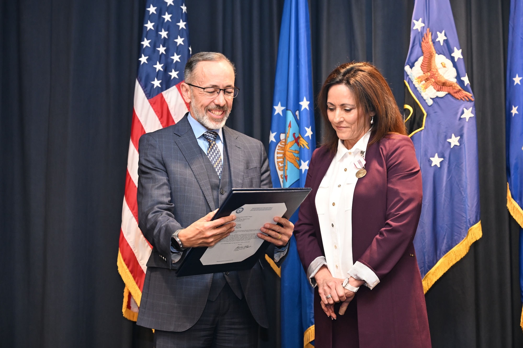 A man in a suit presents a flag in a case to a woman in a suit