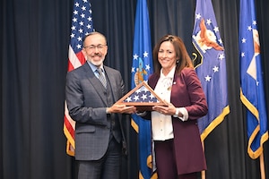 A man in a suit presents a flag in a case to a woman in a suit