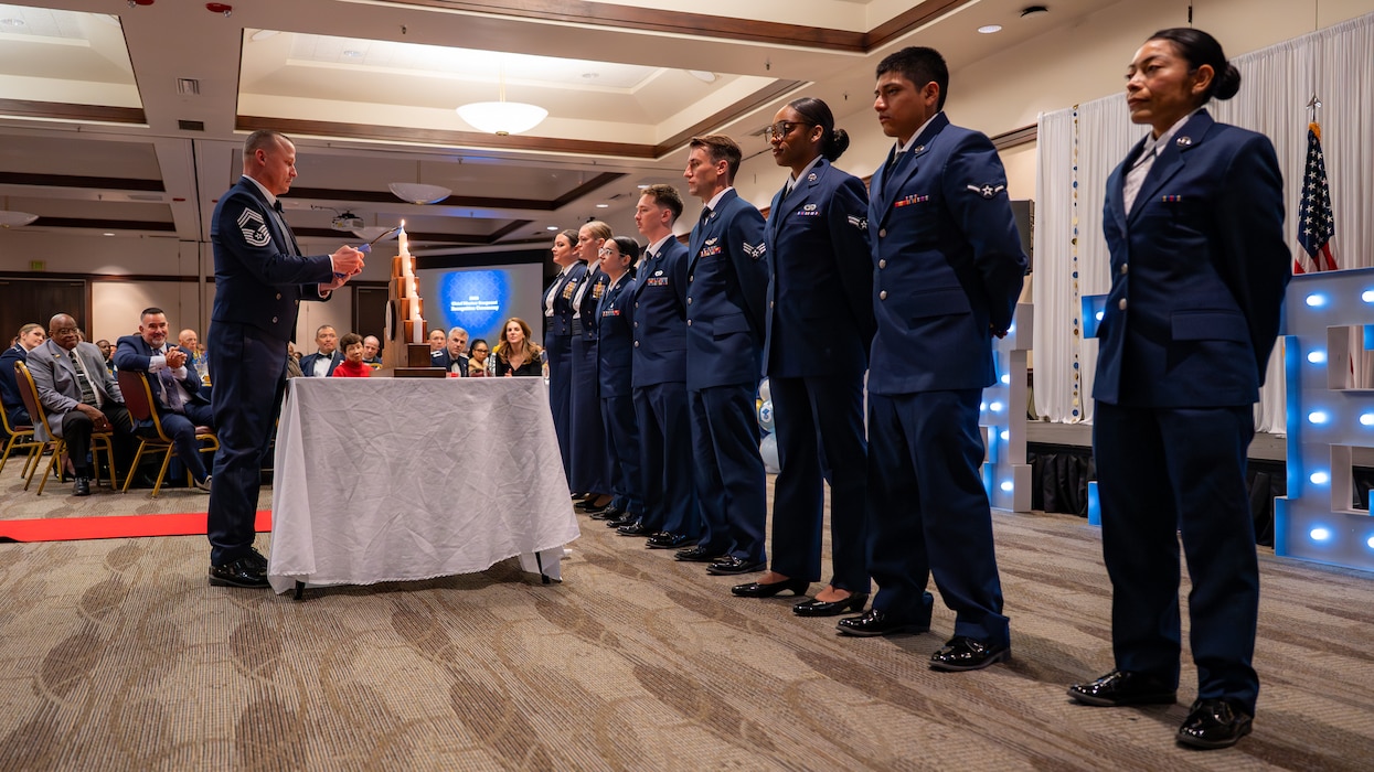 An Airman lights a candle while other Airmen stand in formation to the right