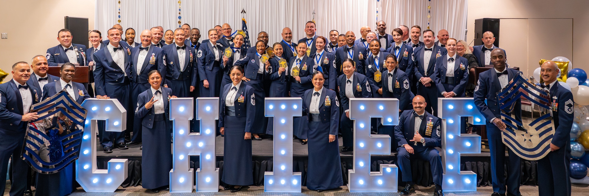 Chiefs gather for a group photo around a big lighted "CHIEF" sign