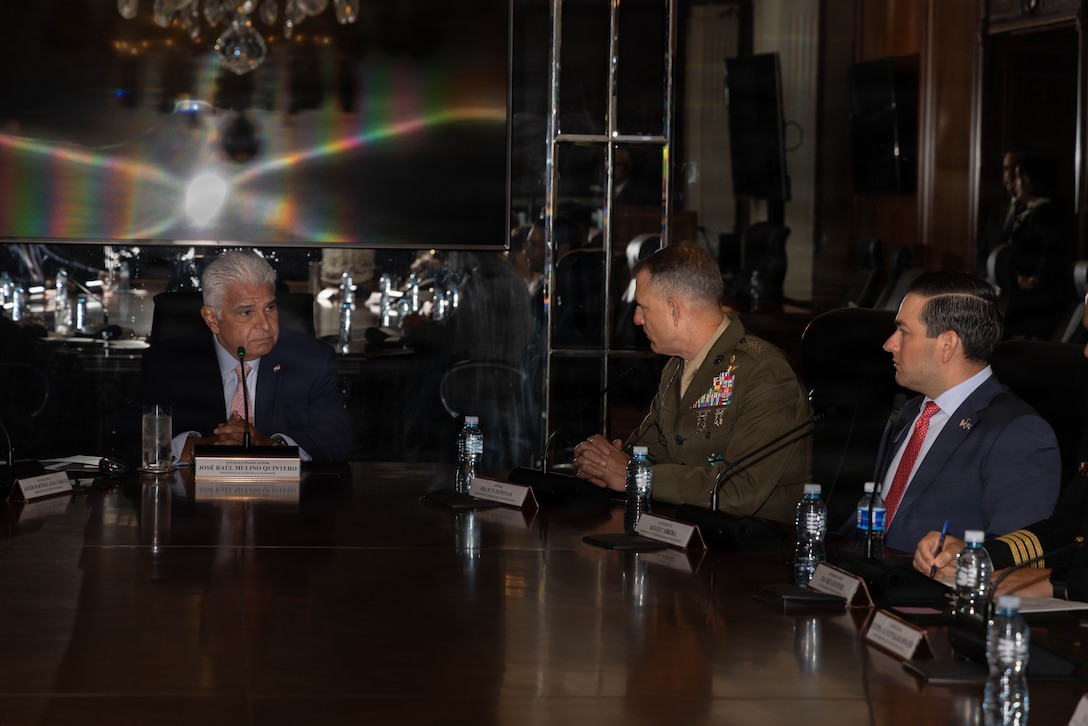 Three men sitting at a table talk to each other.