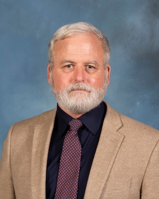 Headshot of Tony Pfaff, USAWC staff, smiling against a neutral background and American Flag.
