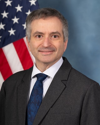Headshot of Edward Kaplan, USAWC staff, smiling against a neutral background and American Flag.