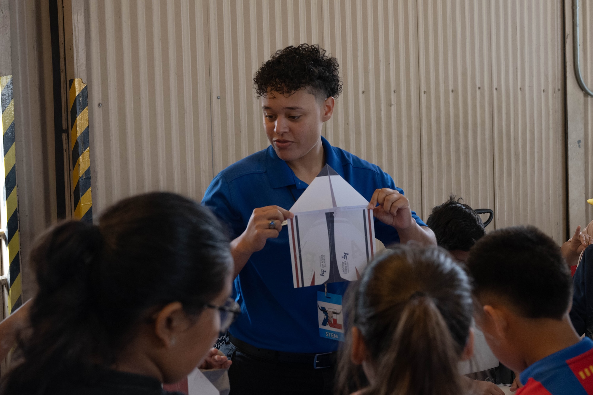 A representative from the U.S. Air Force Academy demonstrates how to create a paper airplane to guests during the Fiesta of Flight STEM Expo at Laughlin Air Force Base, Texas, March 27, 2026. The event allowed guests to discover various STEM-related career opportunities within the Armed Forces and nearby local communities. (U.S. Air Force photo by Airman 1st Class Darryl Keith)