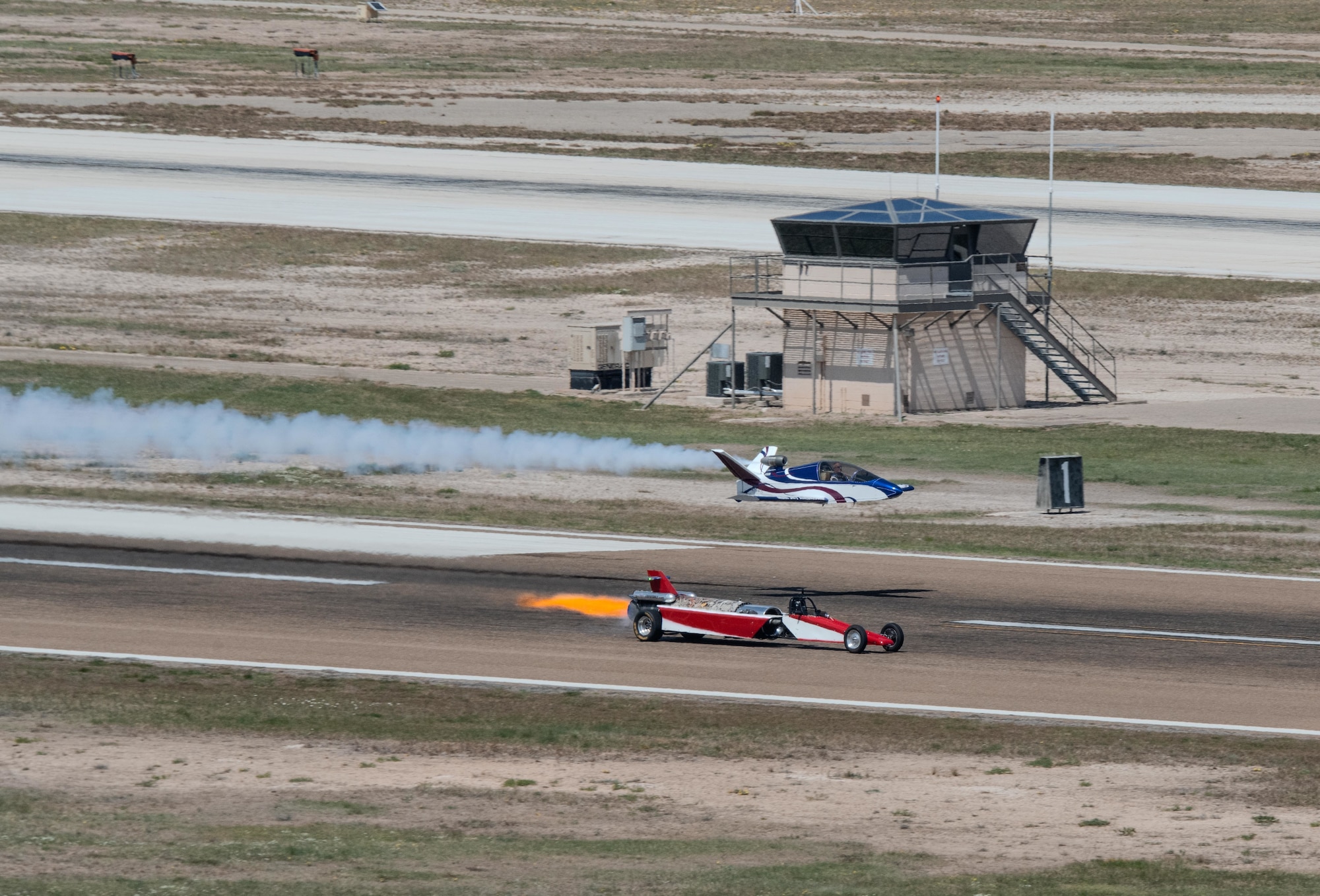 A jet-powered car drag races a mini jet aircraft during a demonstration at the Fiesta of Flight airshow at Laughlin Air Force Base, Texas, March 28, 2026. The performance engaged spectators with a unique combination of aviation and ground-based speed. (U.S. Air Force photo by Airman 1st Class Harrison Sullivan)
