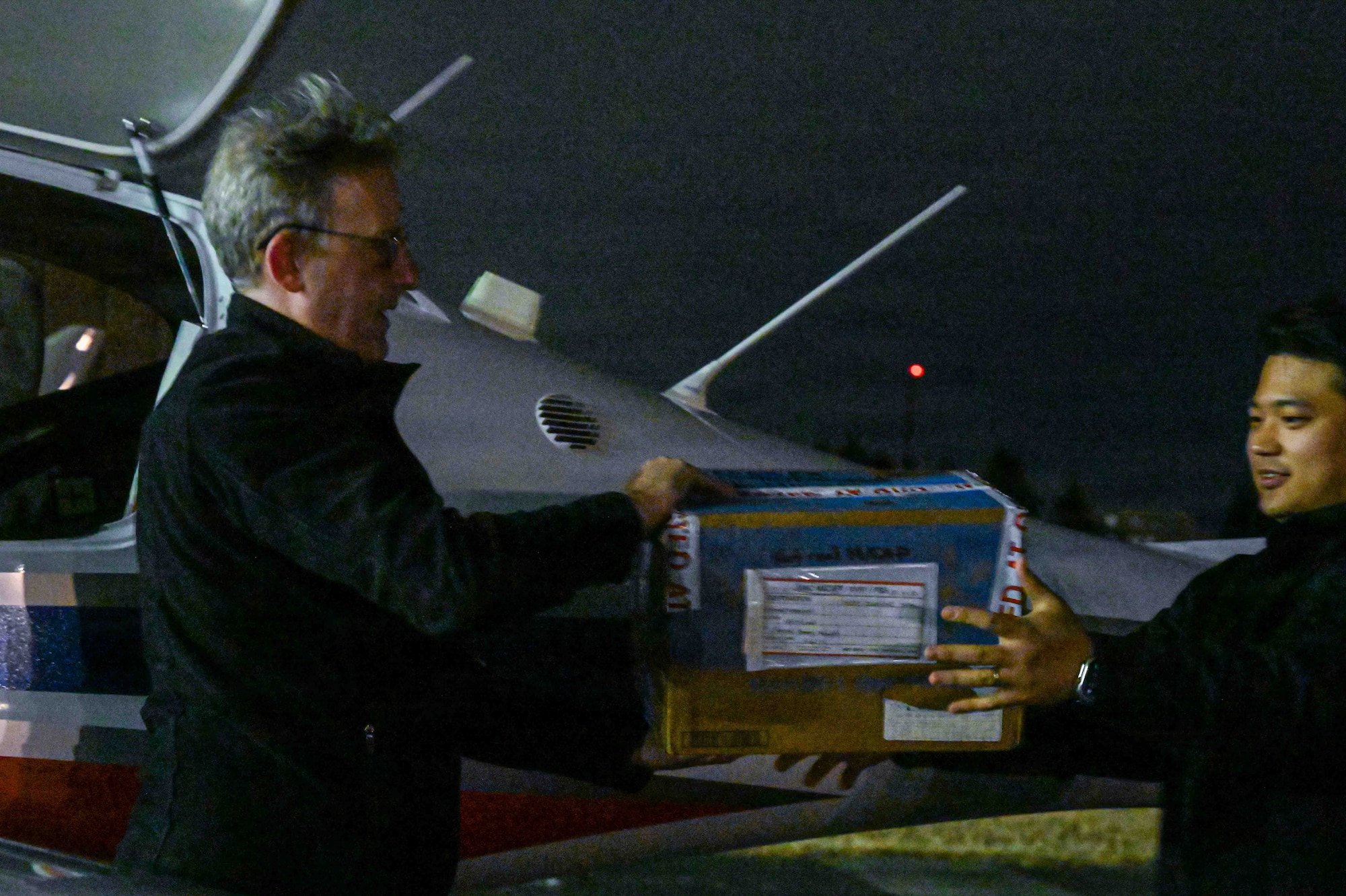 From the left, Jake Kadish, Yokota Flight Center chief instructor, hands simulated repair parts to Michael Shinji Kawashima, YFC assistant chief instructor, during a small parts delivery mission as part of exercise Beverly Midnight 2026 at Yokota Air Base, Japan, March 13, 2026. BM26 provides an optimal environment to enhance and understand possible opportunities to continue the advancement of shared interests.