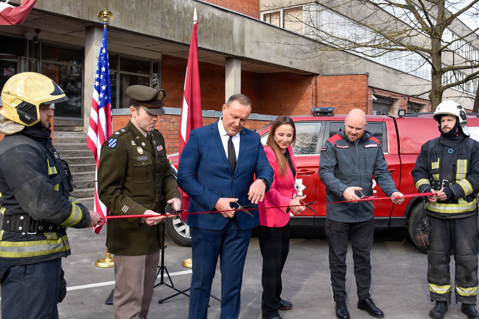 four people, each with a pair of scissors, cutting a ribbon held in front of them by two firefighters.