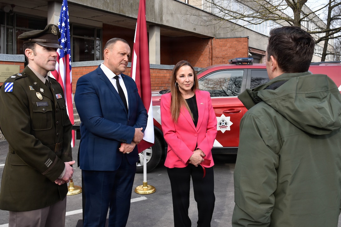 four people standing and talking to each other outside, in front of a building