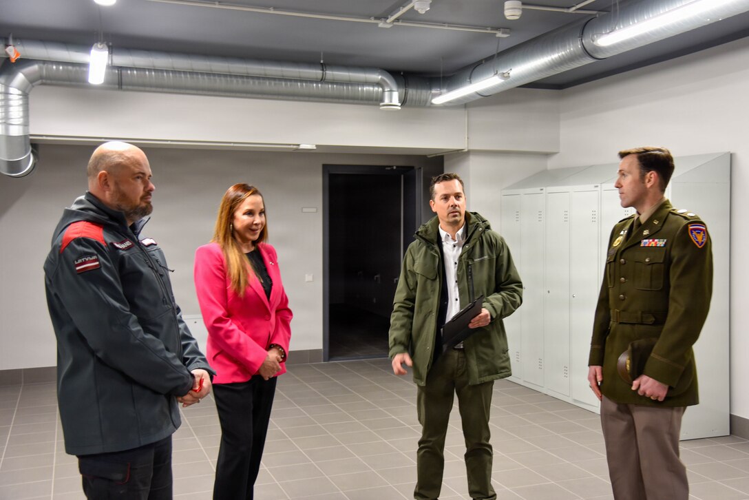 four people standing and talking to each other in an empty room