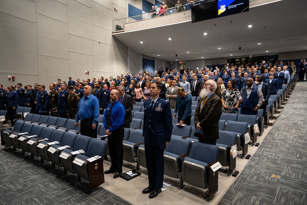 Students from the Air Force Institute of Technology’s Graduate School of Engineering and Management stand for the presentation of the colors at Wright-Patterson Air Force Base, Ohio, March 26, 2026.  The graduating class included 181 students along with international partners from Australia, Saudi Arabia, Chile, Brazil and Israel. (U.S. Air Force photo by Jack Gardner)
