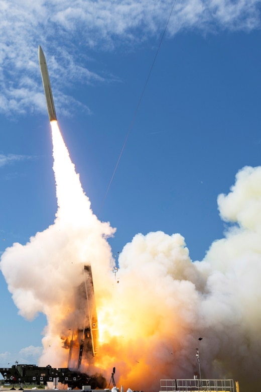 A missile launches during daytime, leaving plumes of smoke and flames behind it as it rises into a blue sky.