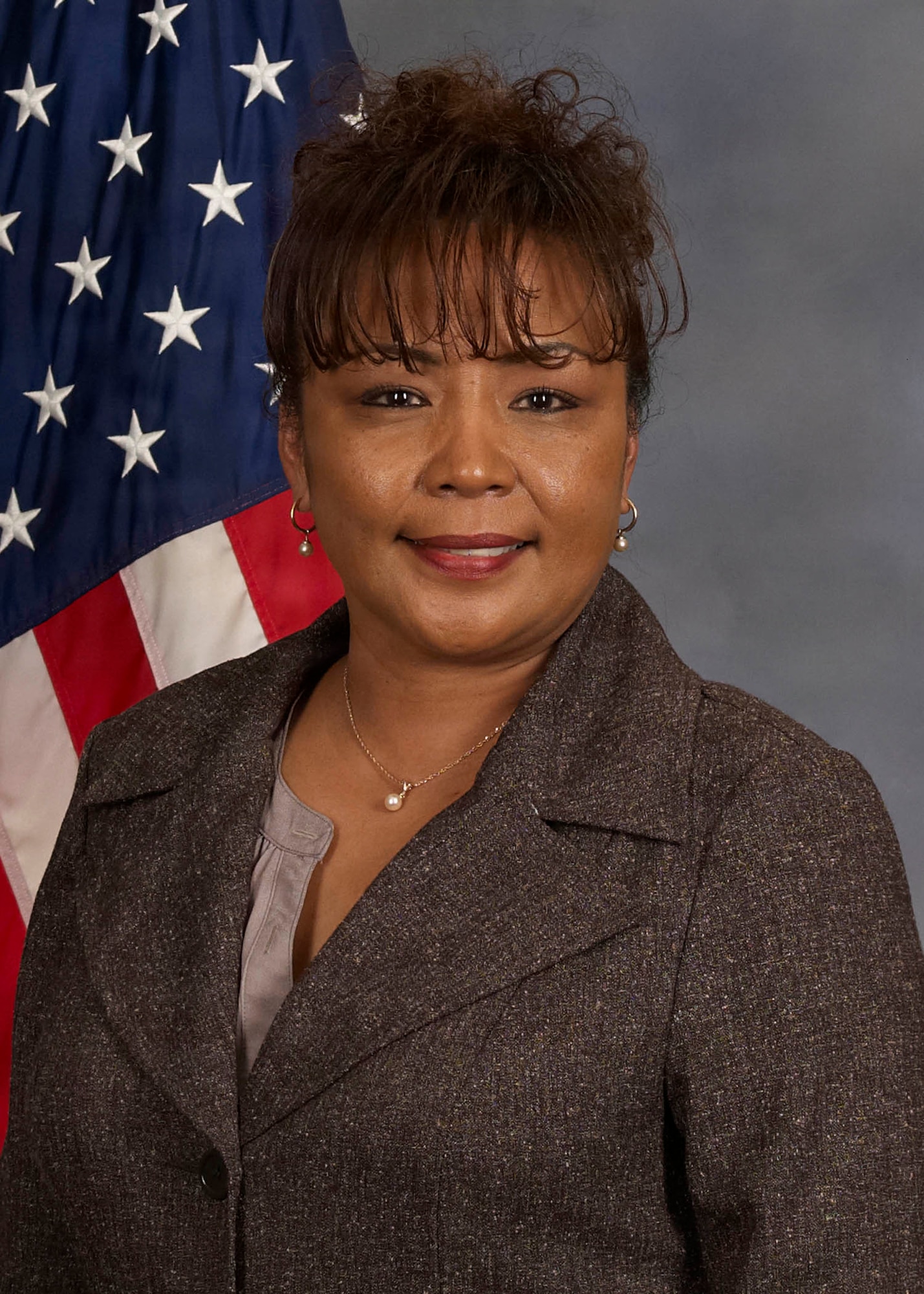 a female in professional attire stares at the camera and smiles. there's an American flag over her right shoulder