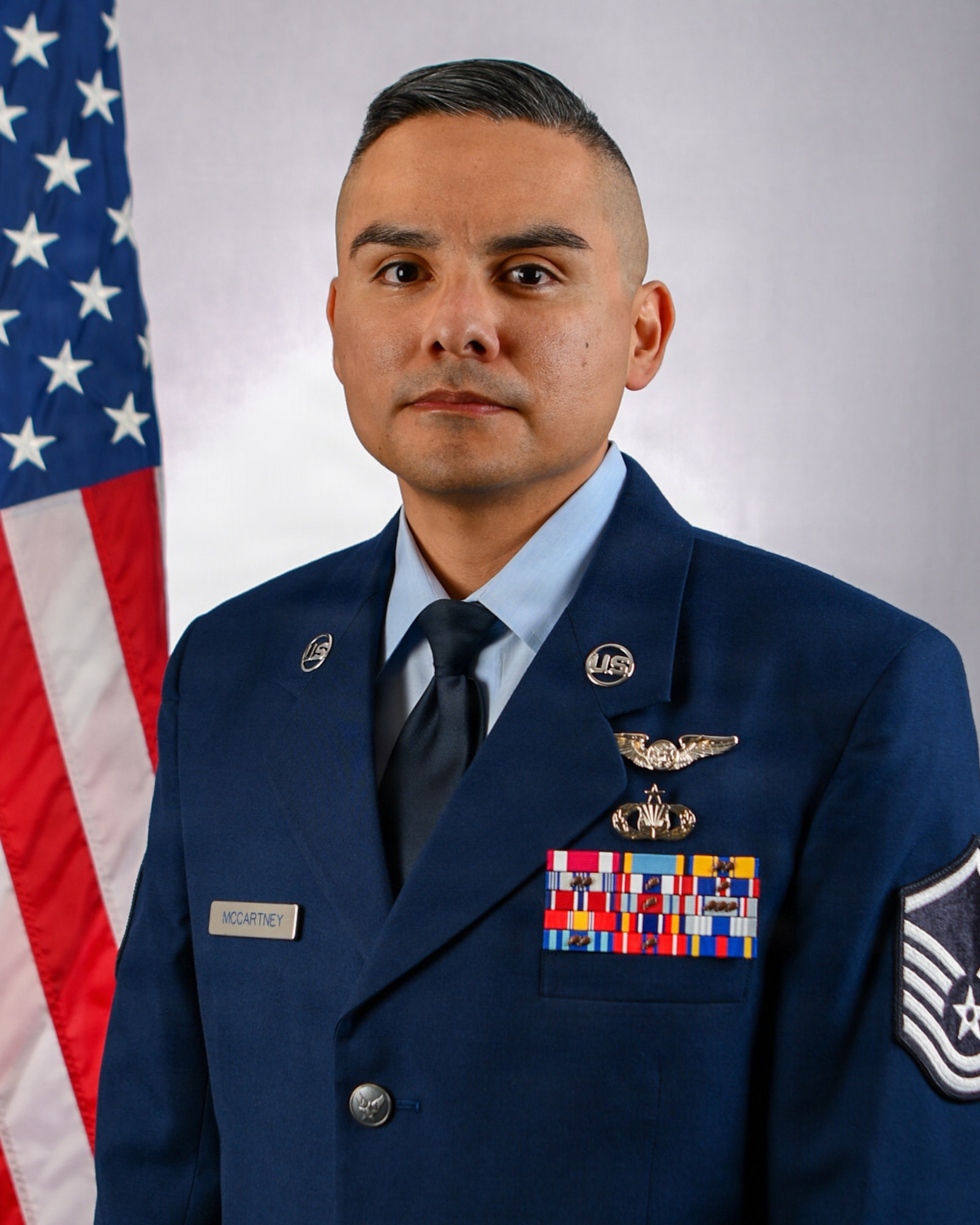 A portrait of a U.S. Air Force male in full service dress with an American flag over his right shoulder