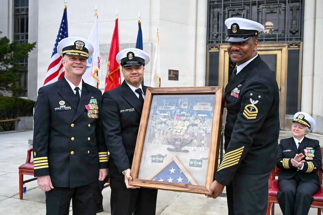 BETHESDA, Md. (Apr. 2, 2026) Command Master Chief Aaron Paul, center, and Master Chief Hospital Corpsman Chevas Watts, senior enlisted leader, Directorate for Surgery, right, Navy Medicine Readiness and Training Command (NMRTC) Bethesda present Capt. Jeffrey Klinger, outgoing commanding officer, NMRTC Bethesda with a gift during a combined change of command and retirement ceremony, at Walter Reed National Military Medical Center, Apr. 2, 2026. NMRTC Bethesda’s mission is to maximize warfighter performance through optimized medical readiness tailored to operational requirements; enhance the readiness of the medical force to sustain expeditionary medical capability; and train and develop the Navy Medicine Force. (U.S. Navy photo Mass Communication Specialist Second Class Alec Kramer)