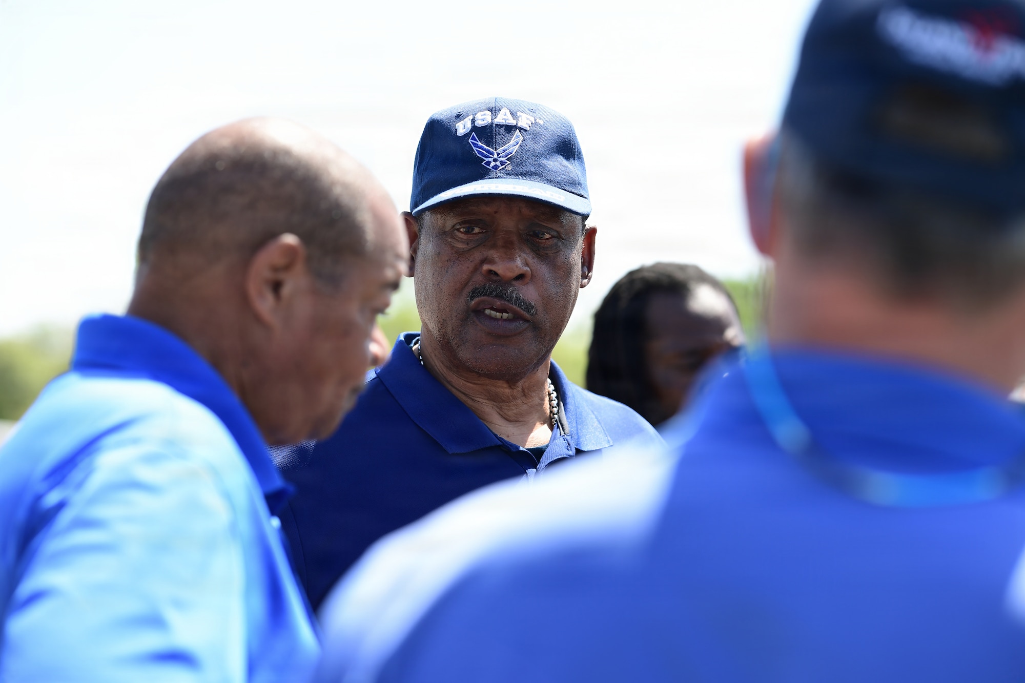 A man wearing blue speaks to a group of people.