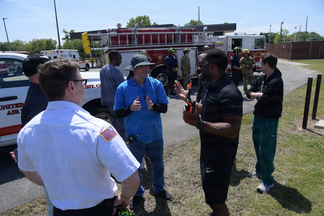 A group of emergency responders gather together to discuss the training scenario in front of a fire truck.