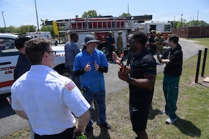 A group of emergency responders gather together to discuss the training scenario in front of a fire truck.