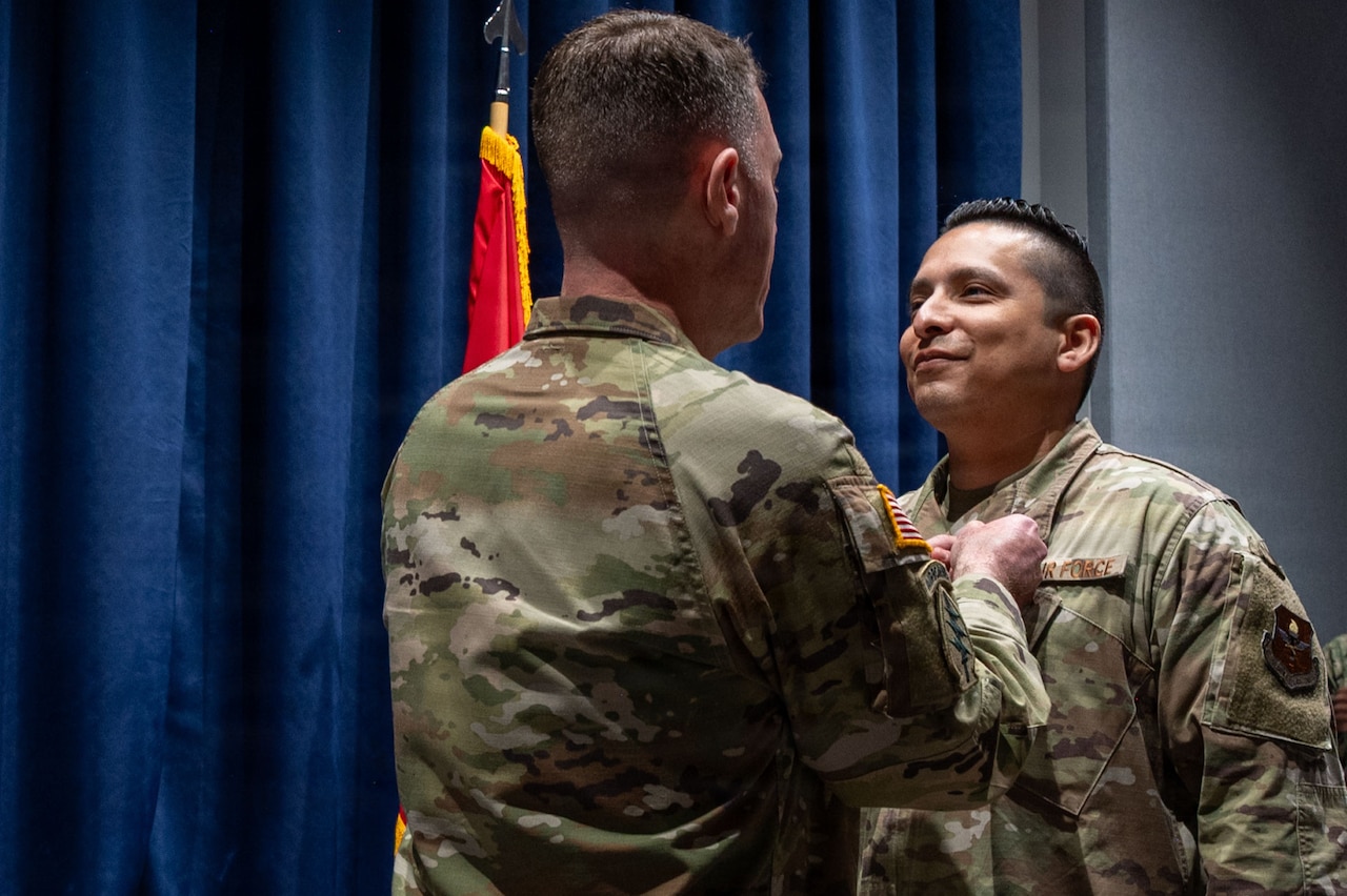 A man in a camouflage military uniform pins an award on a man in similar attire.