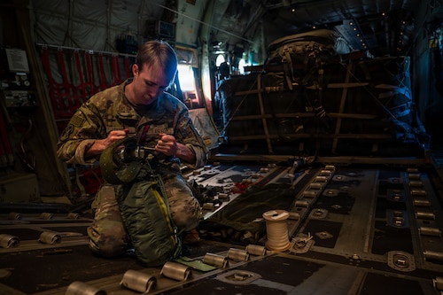 A member configuring a parachute in the back of an aircraft