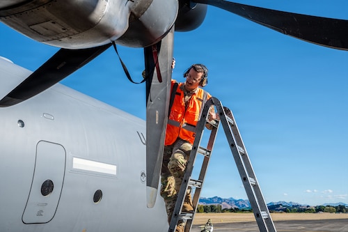An Airman on a ladder inspecting the propeller blades of an aircraft