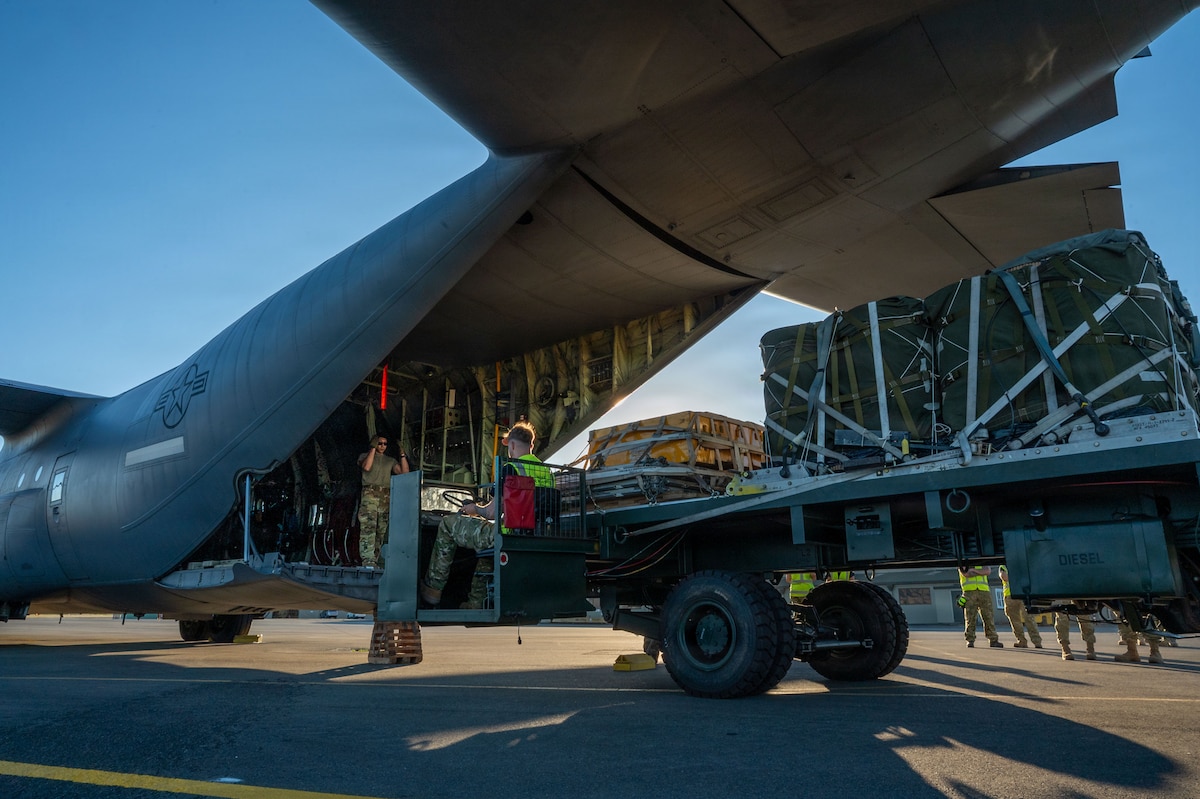 A large cargo trolley transports cargo bundles into the back of a C-130J aircraft
