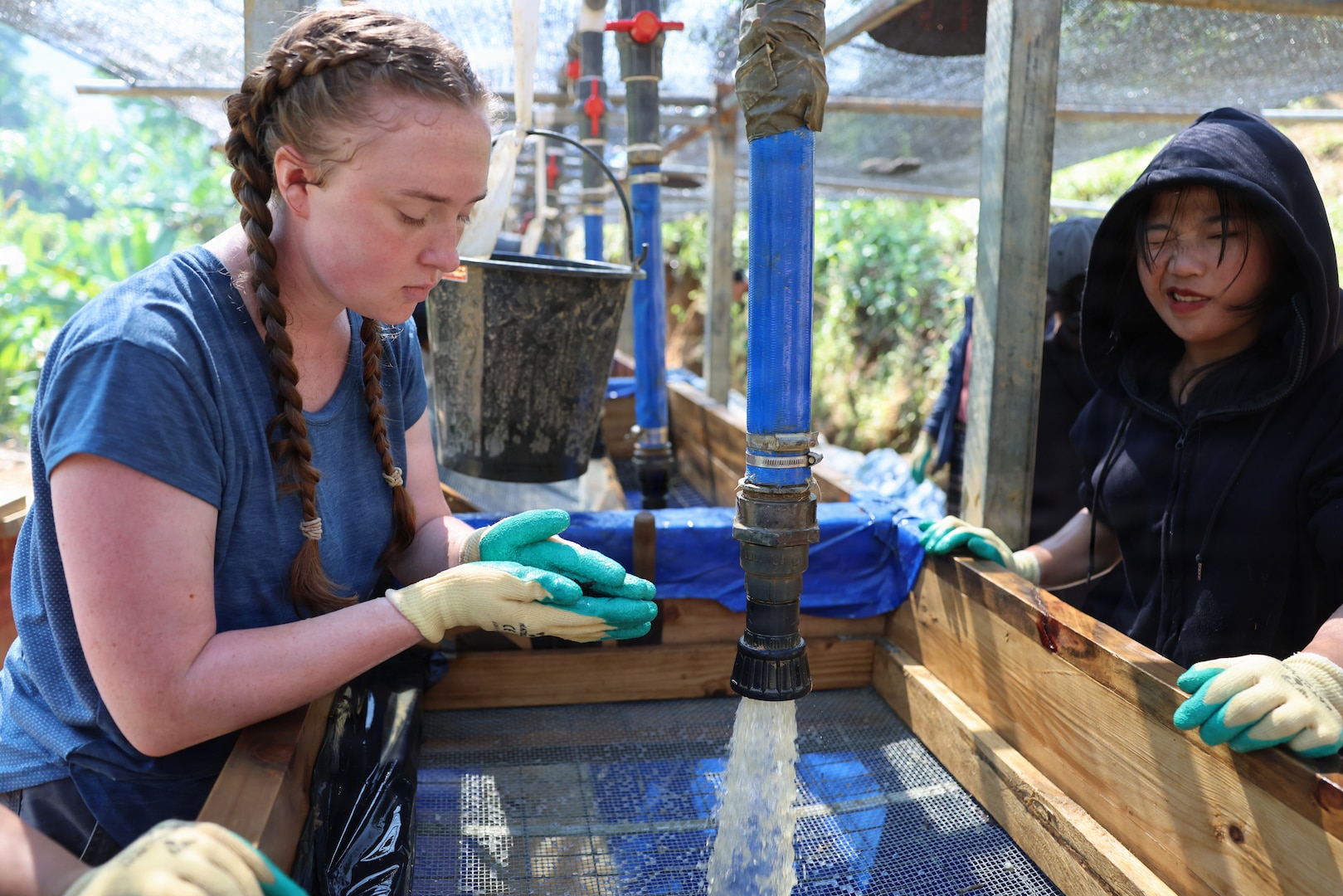 U.S. Navy Hospital Corpsman 3rd Class Brooklyn Purdy, a medic for Recovery Team 3, part of Defense POW/MIA Accounting Agency Joint Field Activity 26-3LA, examines potential evidence while wet-screening with local Lao workers at a recovery site in Laos, March 27, 2026.